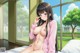 A naked anime girl sitting on a bed in front of a window.