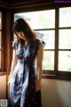 A woman standing in front of a window wearing a dress.