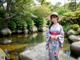 A woman in a kimono and hat standing by a stream.