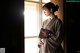 A woman in a kimono standing by a window holding a book.